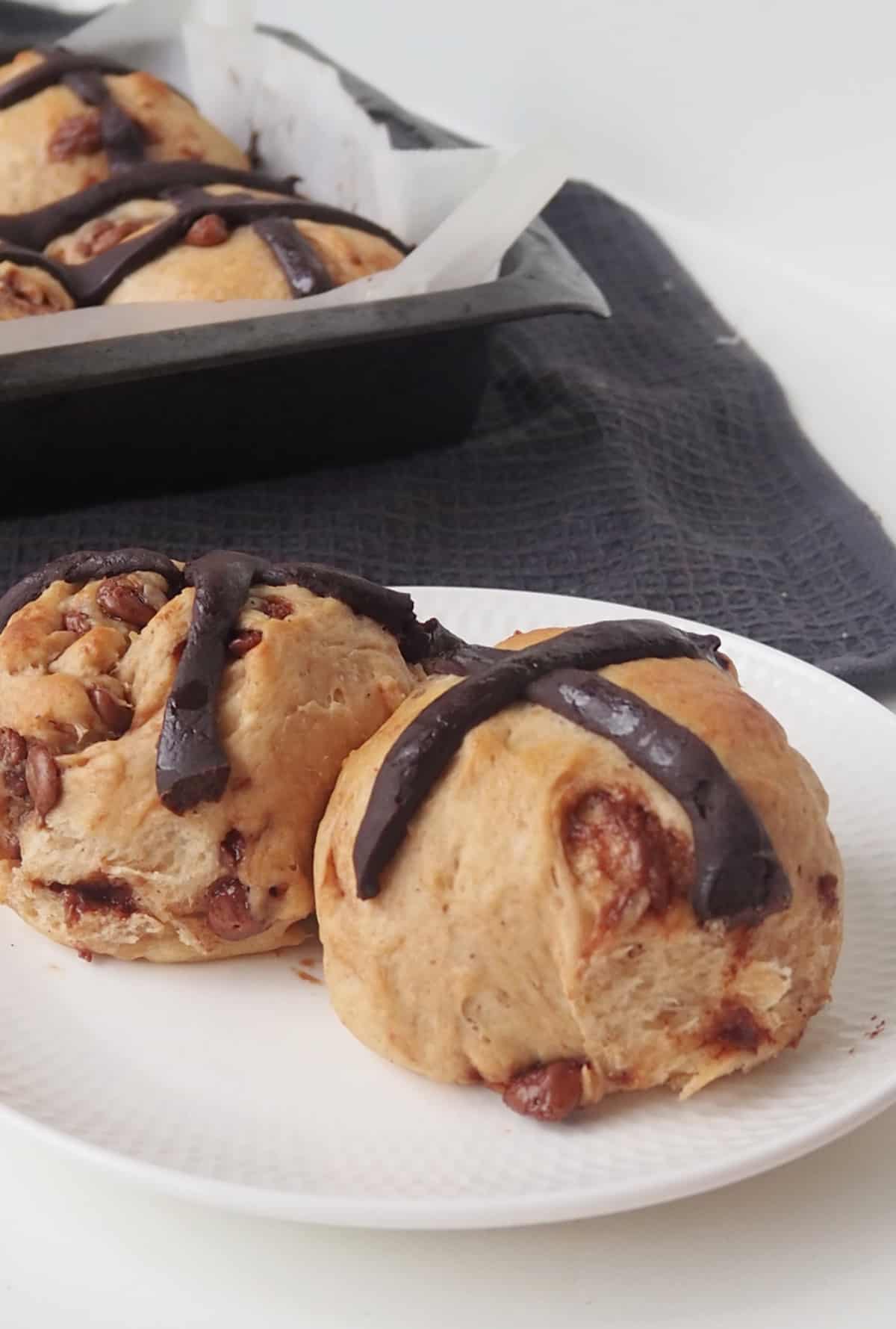 Two Chocolate Chip Hot Cross Buns on a white plate.