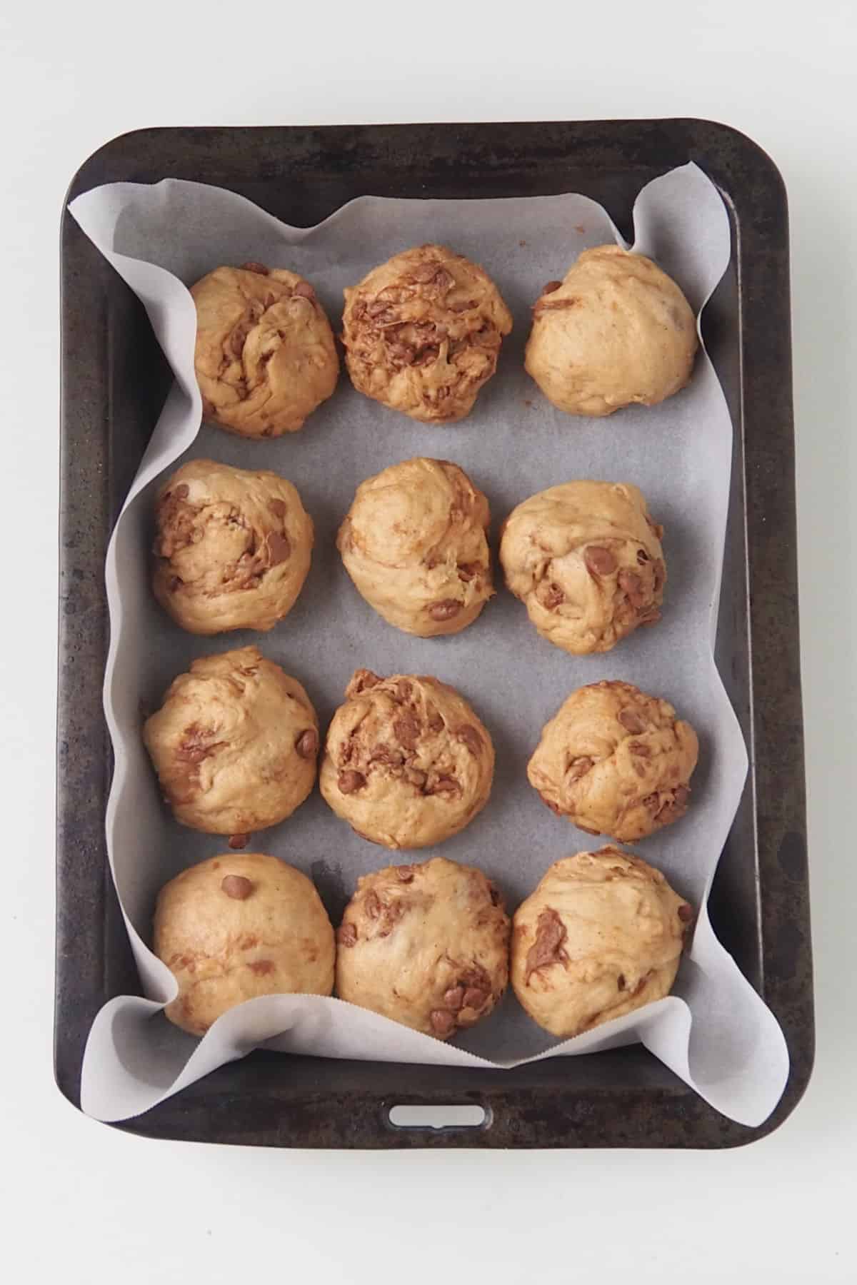 Chocolate Chip Hot Cross Buns on a baking tray.