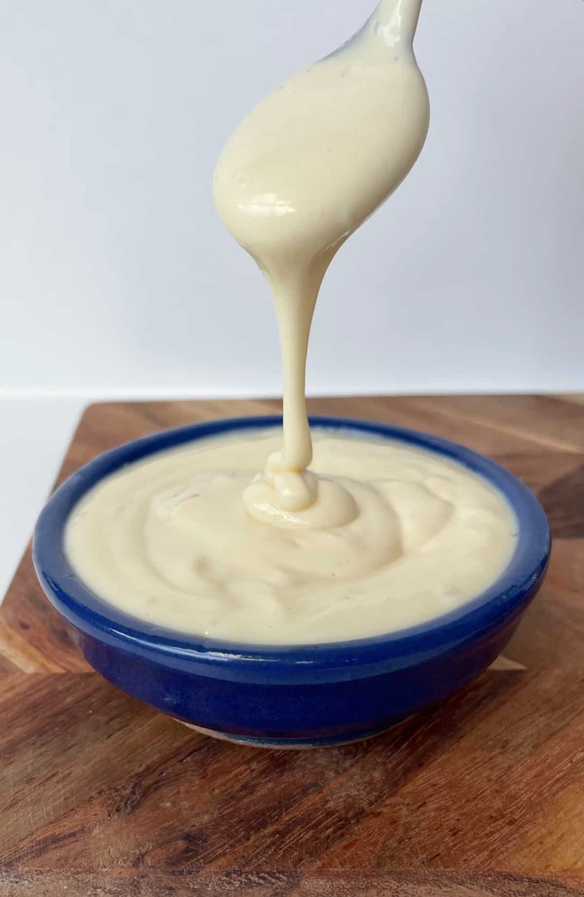 Mayonnaise being drizzled into a small blue bowl from a spoon.
