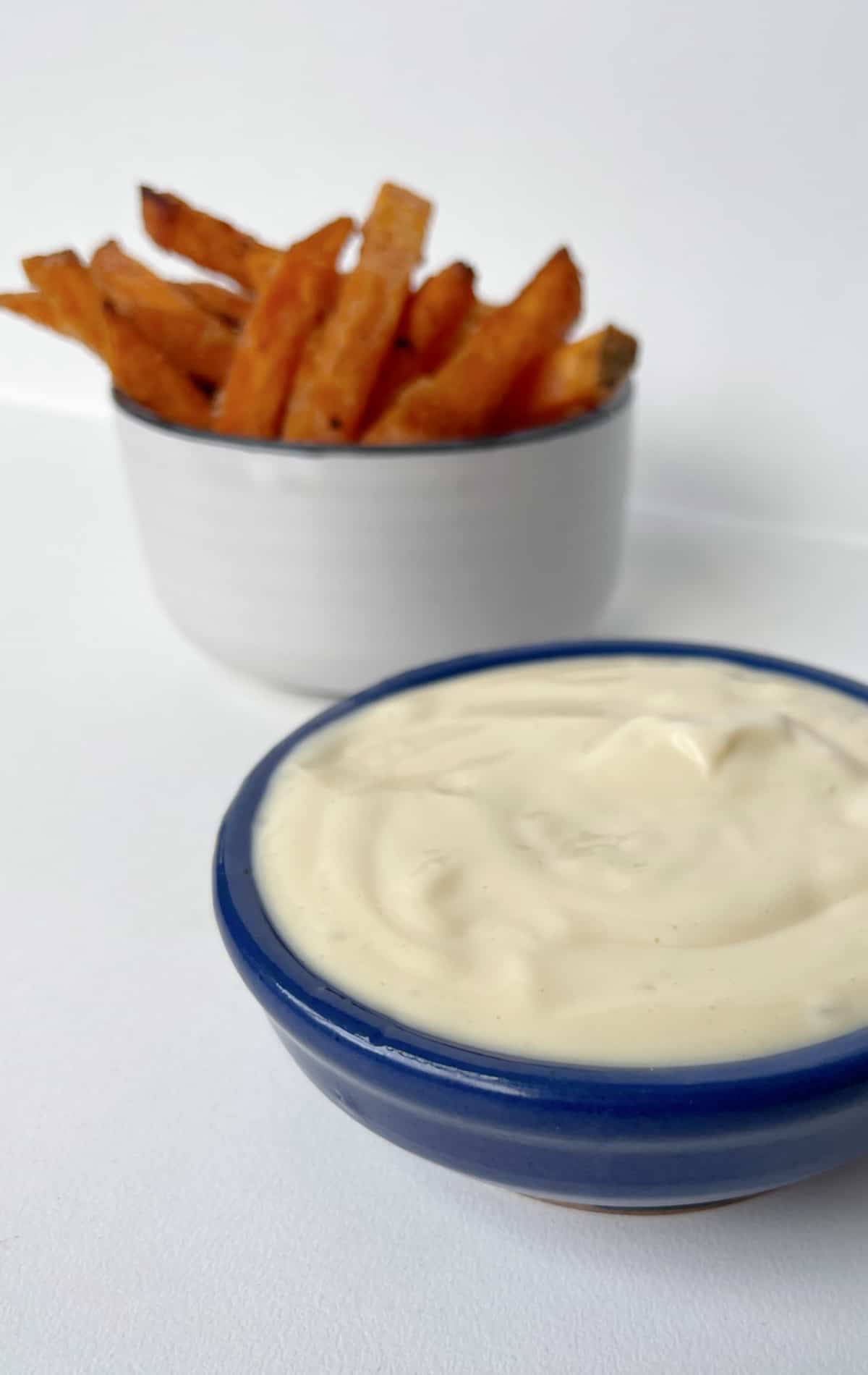 A bowl of mayonnaise sitting in front of a bowl of sweet potato chips.