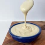 Mayonnaise being drizzled into a small blue bowl from a spoon.