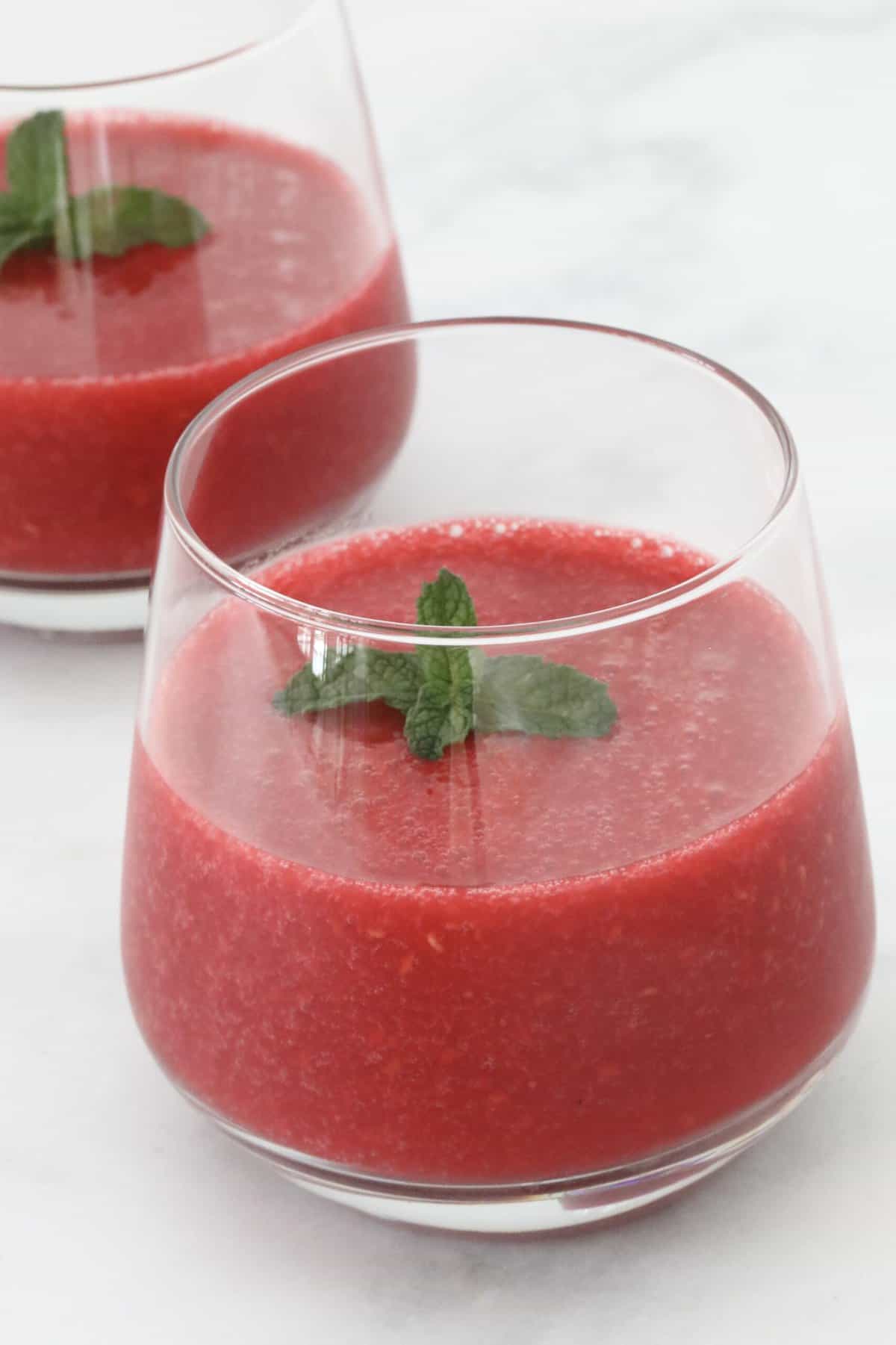 A glass filled with a red fruit drink and fresh mint.