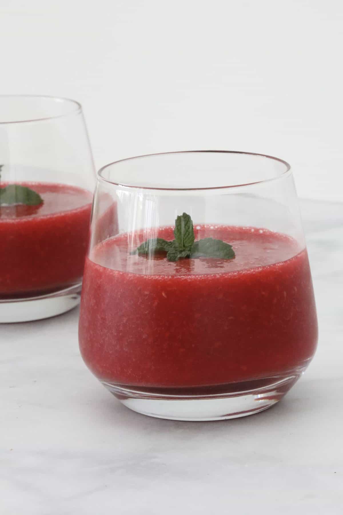 Glasses filled with raspberry drink and mint leaves.