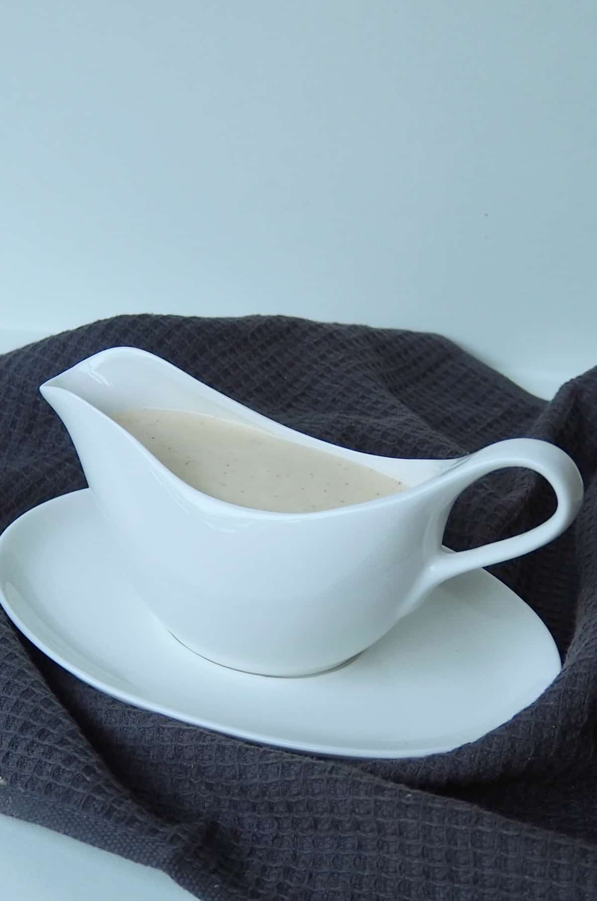Cheese sauce in a white jug on a dark grey tea towel.
