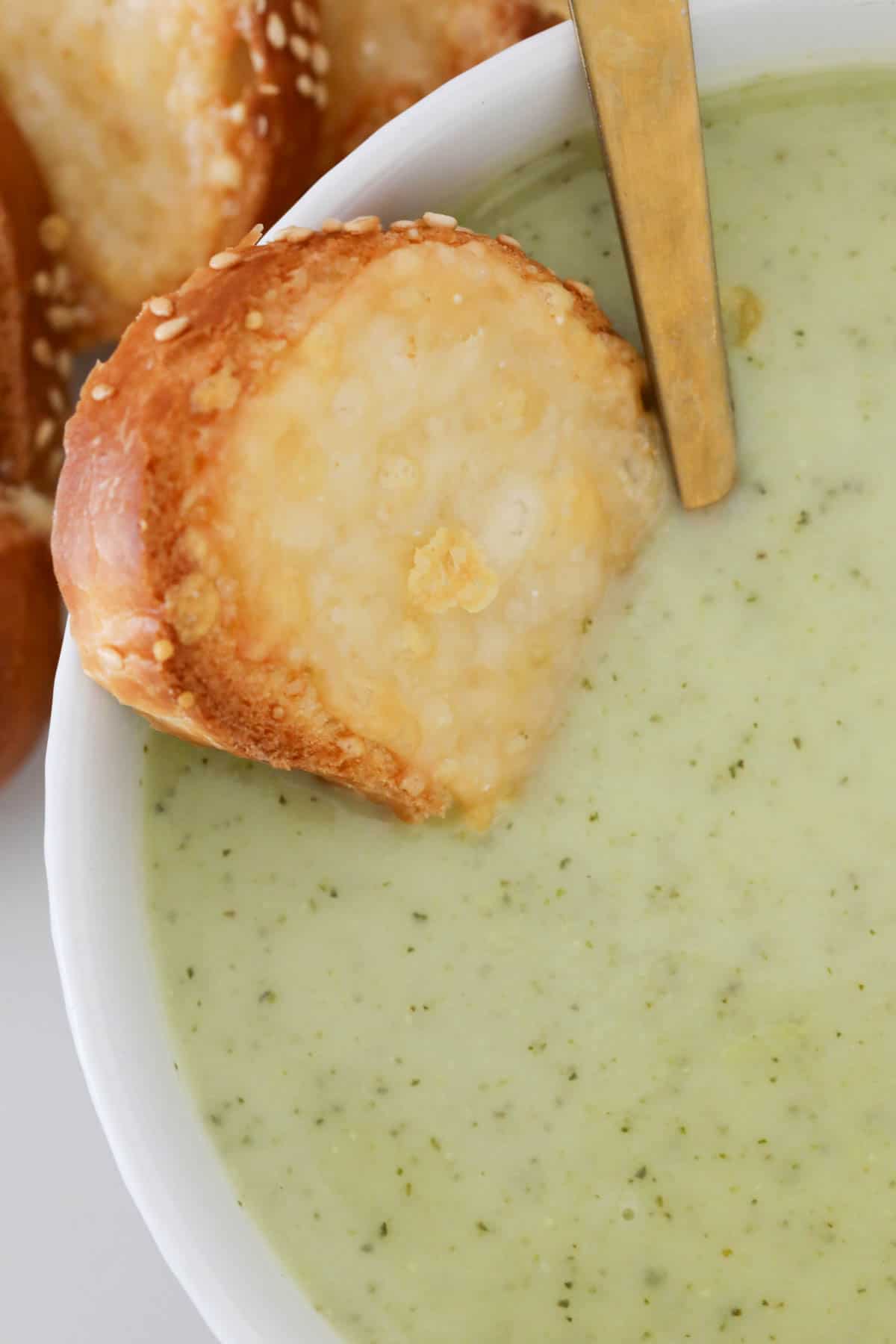 A piece of cheesy bread dipped into zucchini soup.