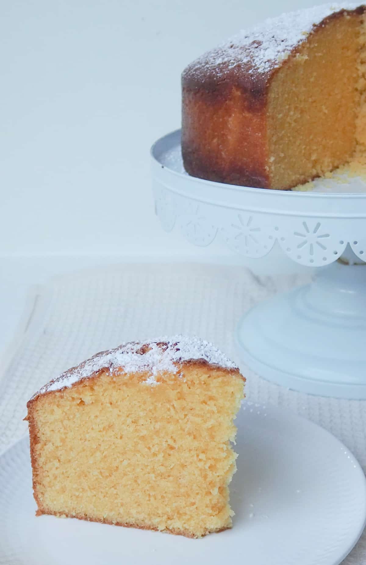 Slice of custard cake on a white plate. in the background is the custard cake on a white serving platter.