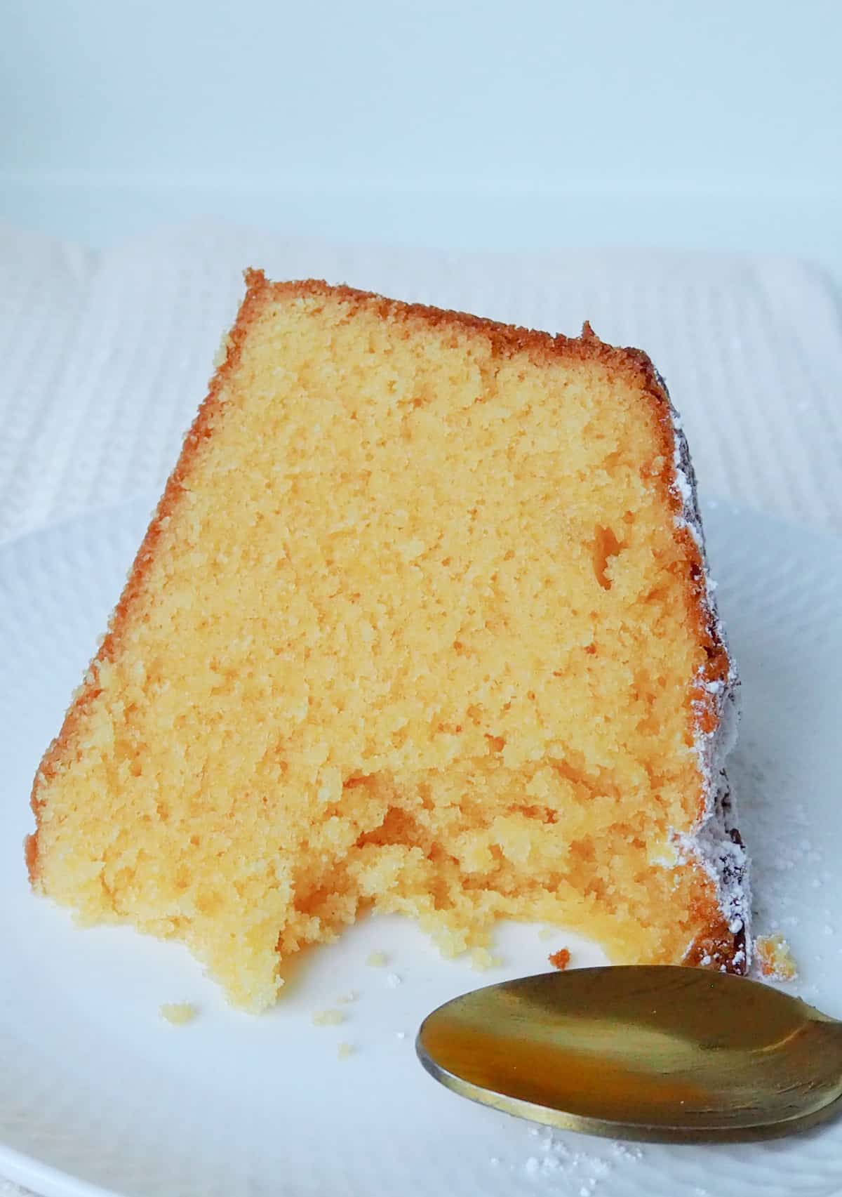 Slice of custard cake with a piece removed on a white plate. There is a gold spoon sitting next to it.
