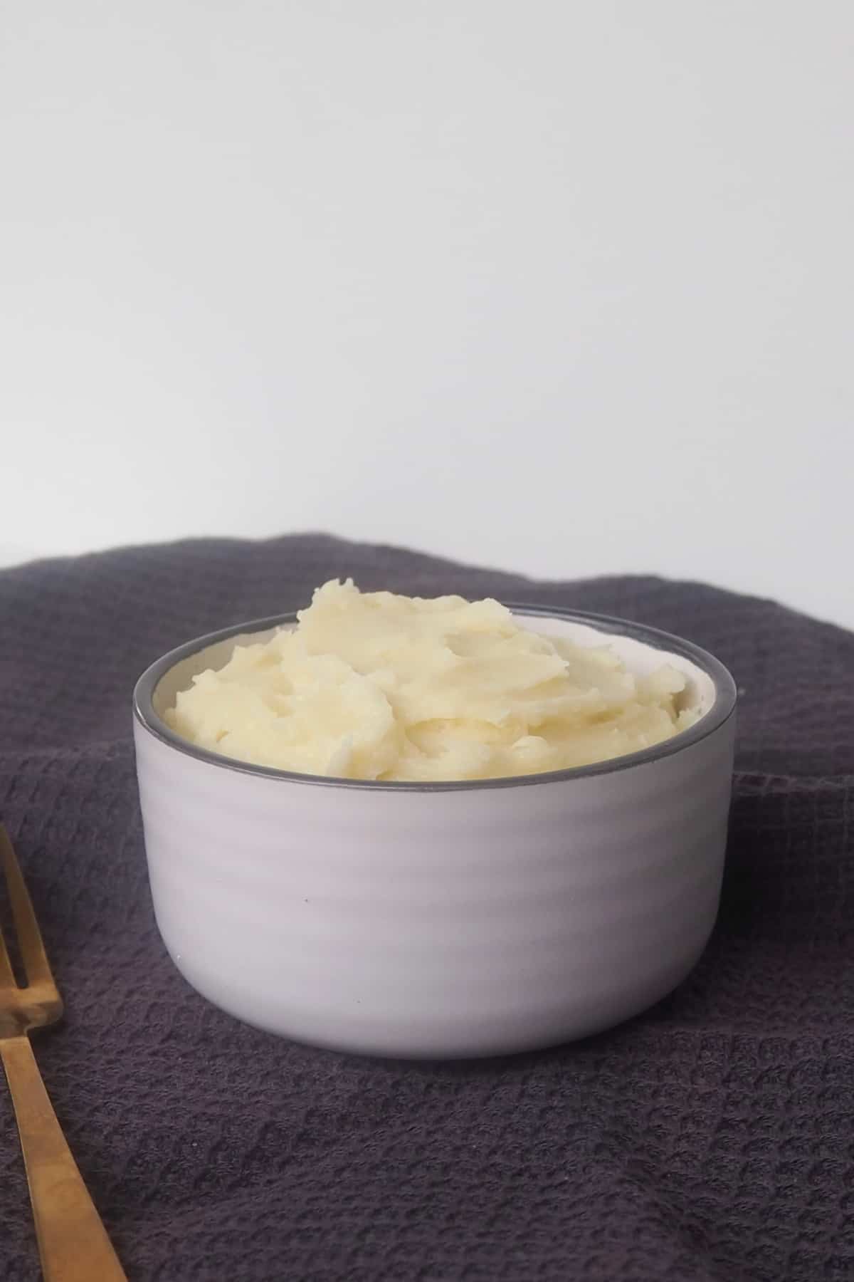 side view of mashed potatoes in a white bowl sitting on top of a dark grey towel.
