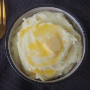 Overhead view of mashed potatoes in a white bowl. There is melted butter dripping down the sides.