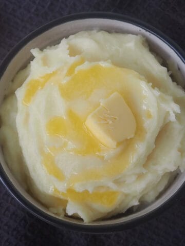 Overhead view of mashed potatoes in a white bowl. There is melted butter dripping down the sides.