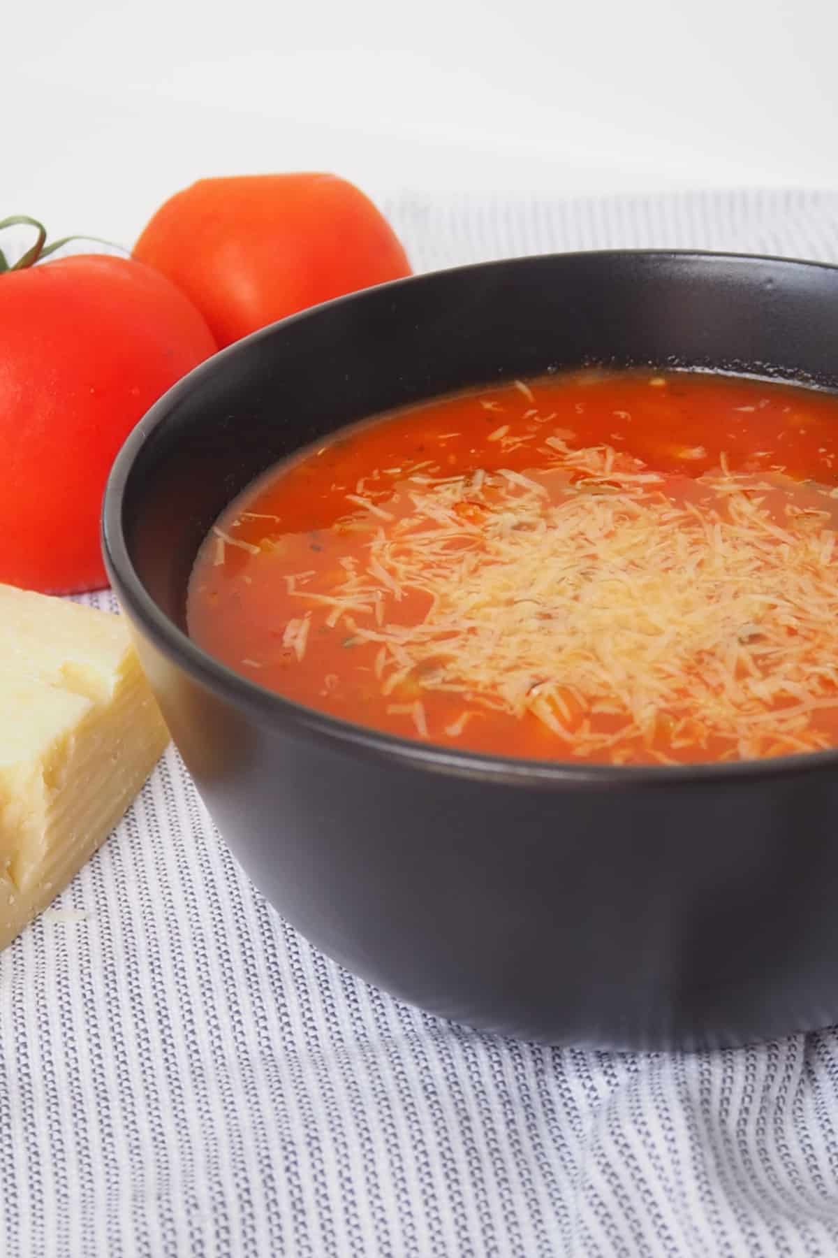 Side view of Spicy Tomato Soup in a black bowl that is topped with grated parmesan cheese.