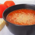 Side view of Spicy Tomato Soup in a black bowl that is topped with grated parmesan cheese.
