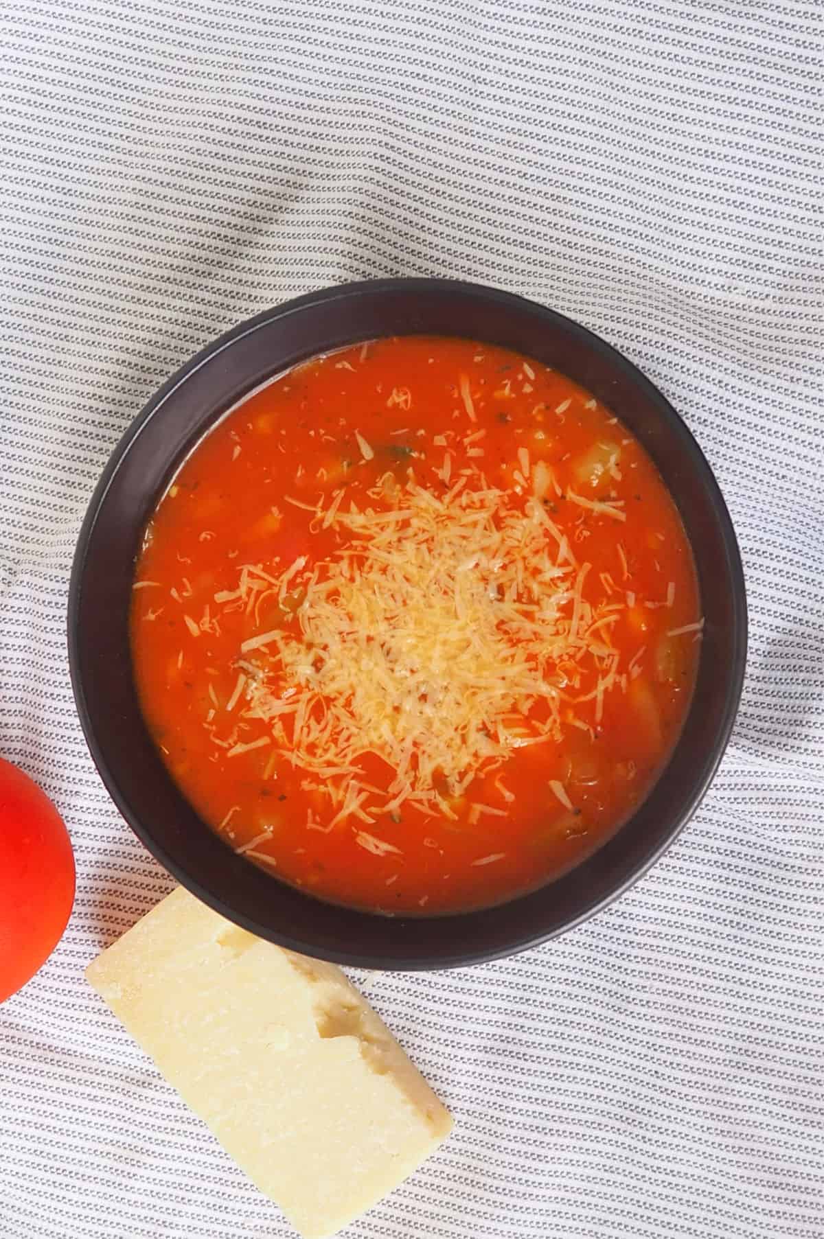Overhead view of Thermomix Spicy Tomato Soup in a black bowl topped with grated parmesan cheese.