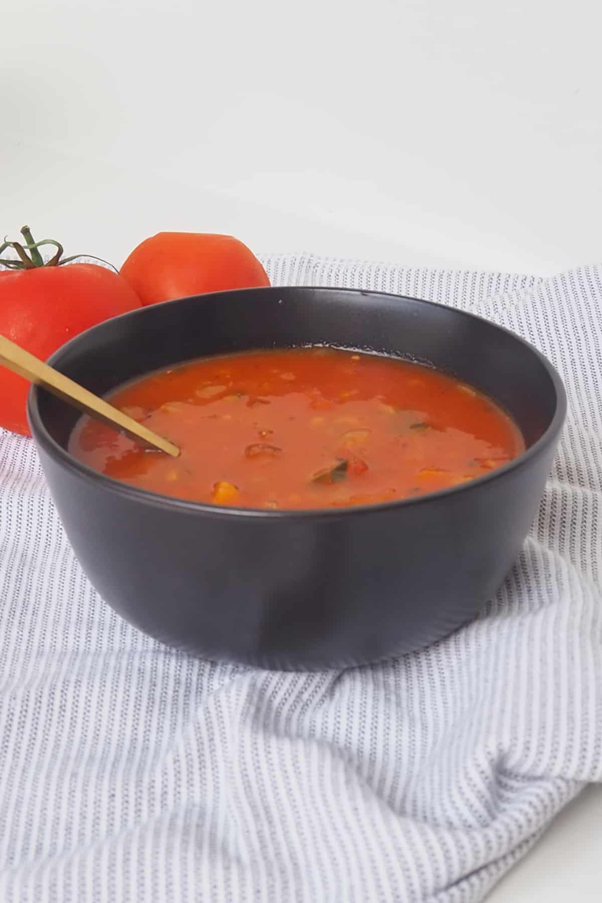 Side view of Spicy Tomato Soup in a black bowl. there is a gold spoon sitting in the bowl.