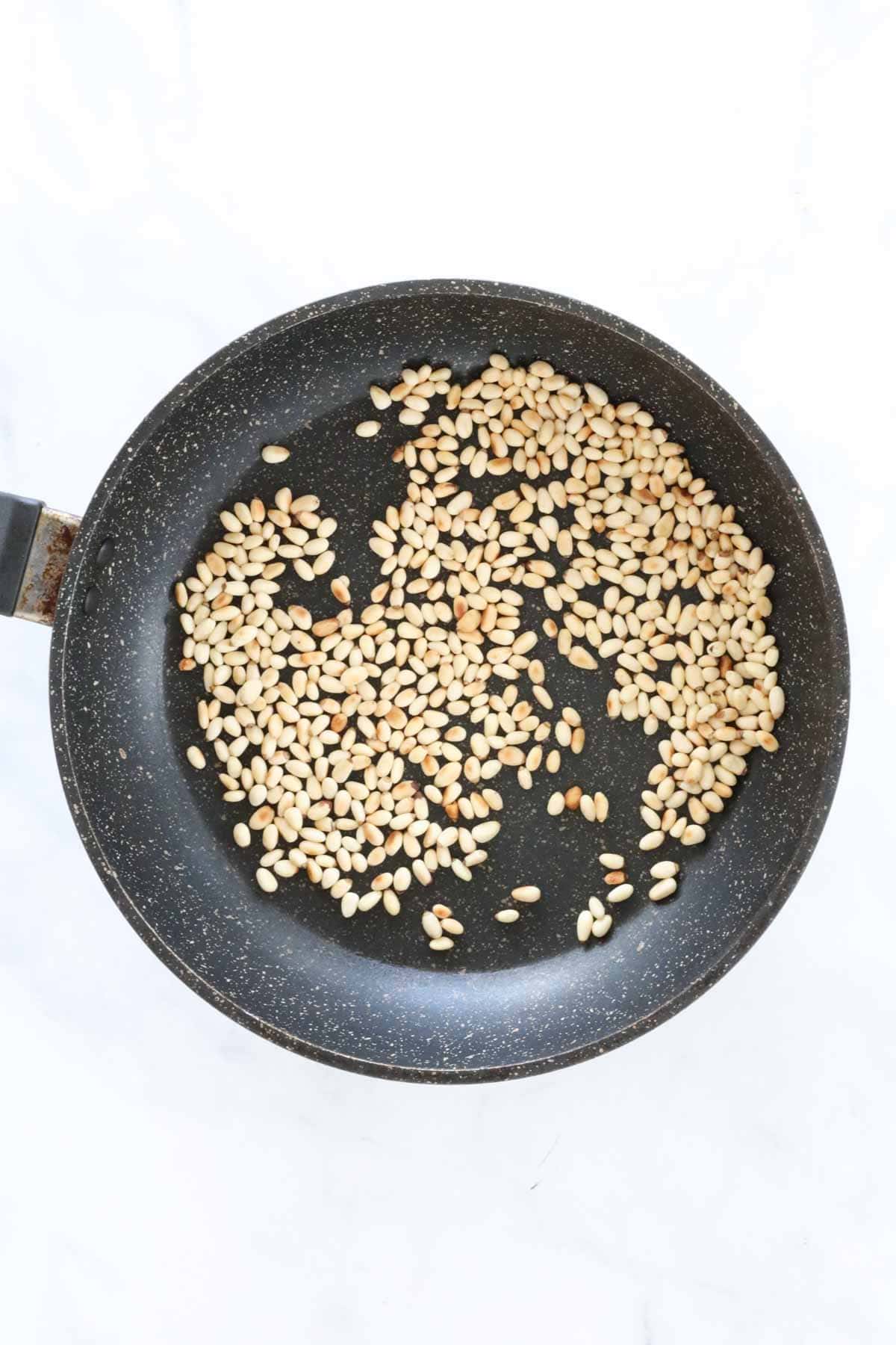 Pine nuts being toasted in a frying pan.