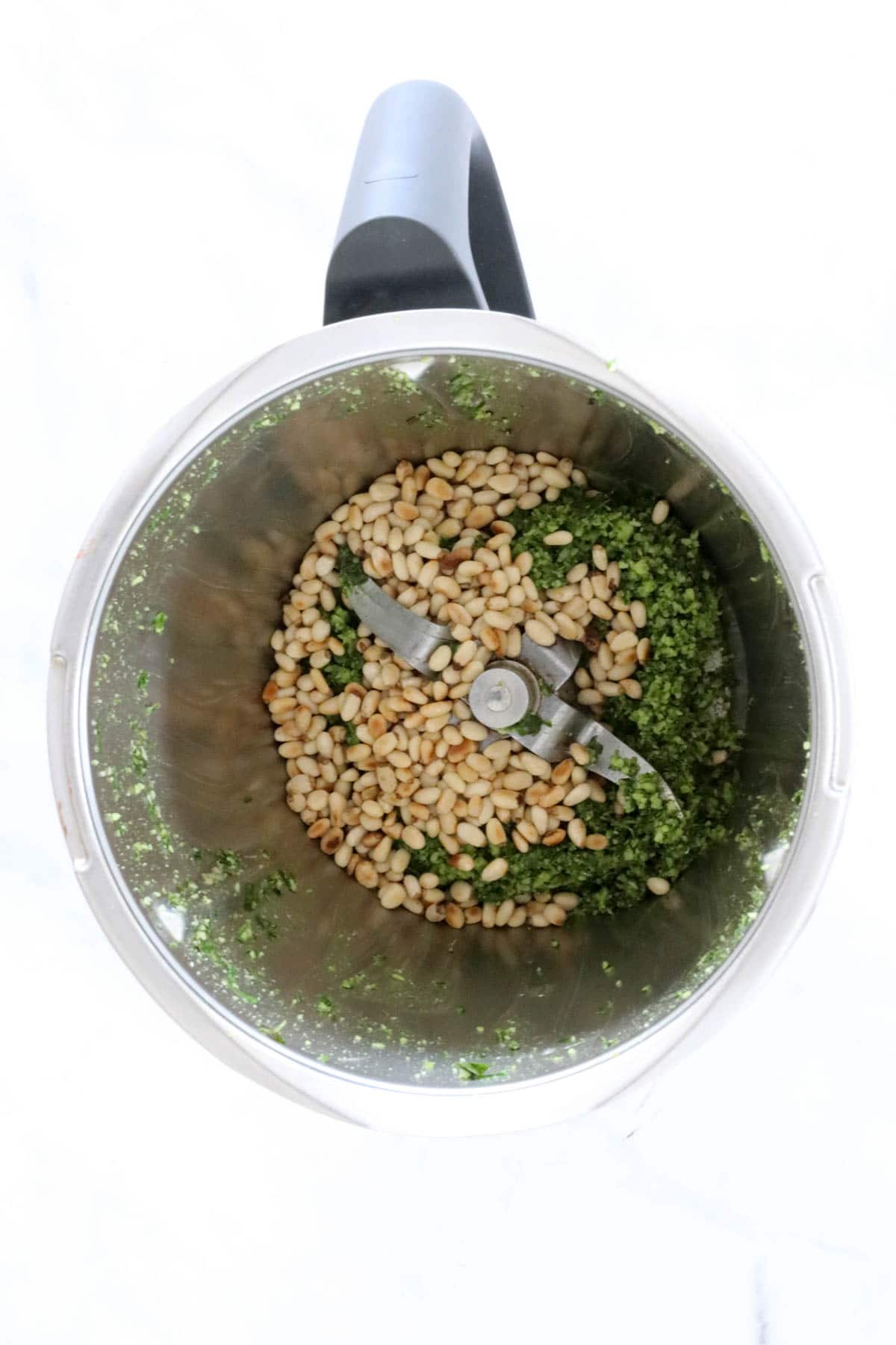 Pine nuts on top of green mixture in a Thermomix.