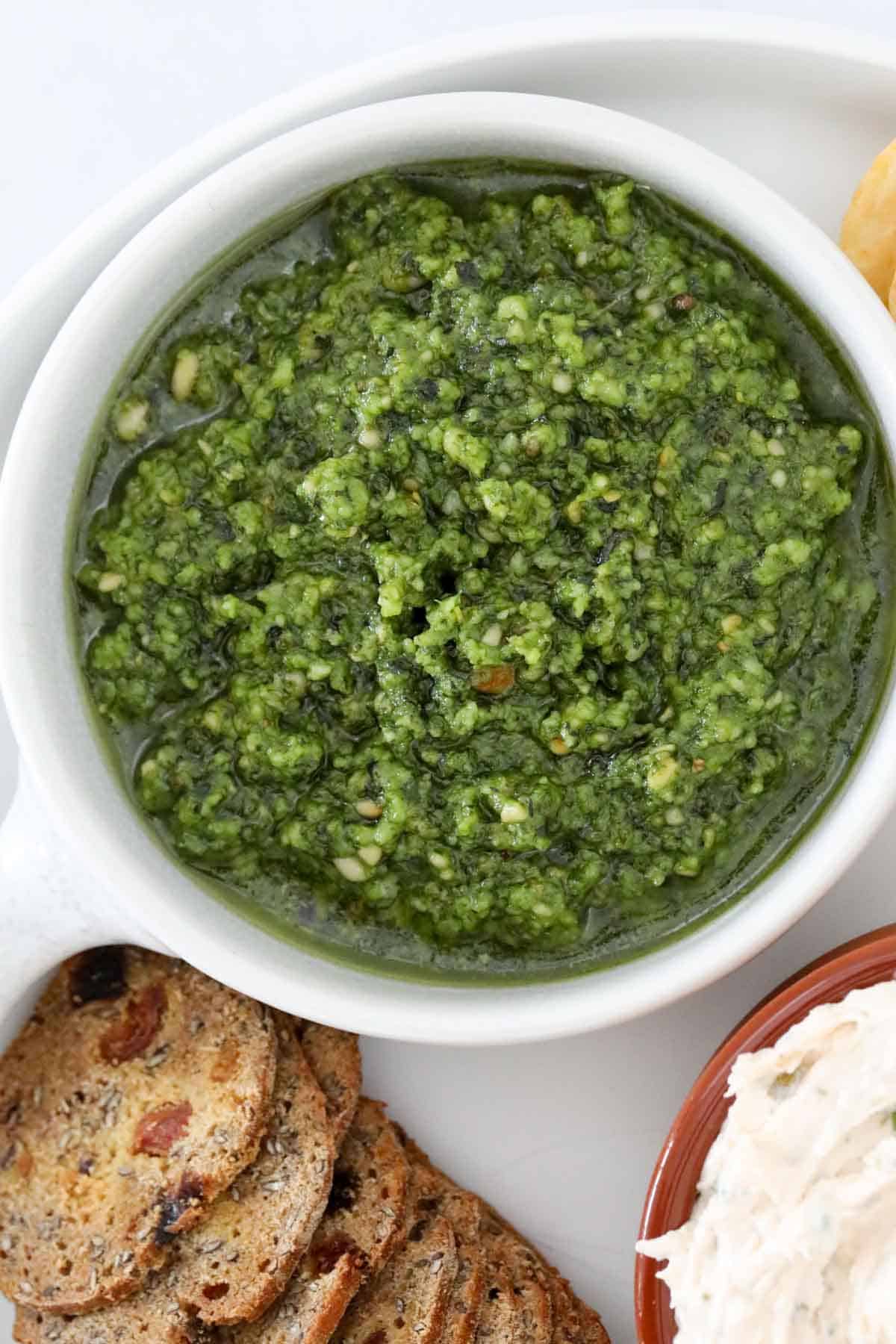 An overhead shot of a bowl of basil pesto and crackers.