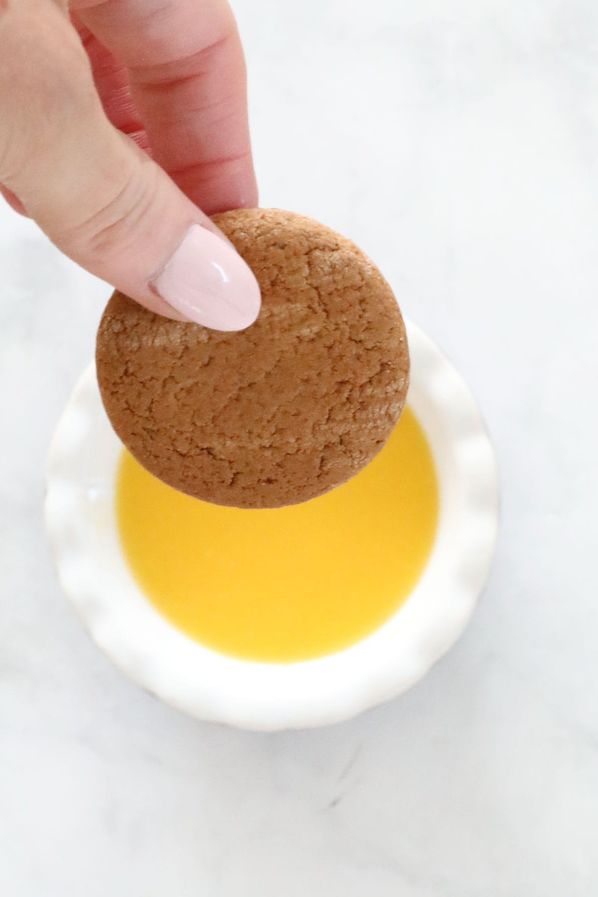 A gingernut biscuit being dipped into orange juice.