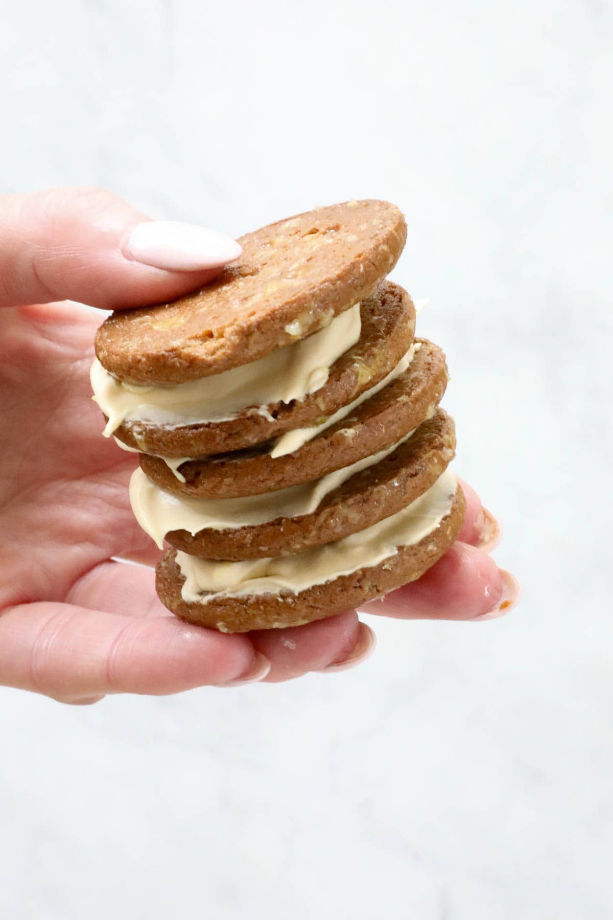 A hand holding biscuits sandwiched in whipped cream.