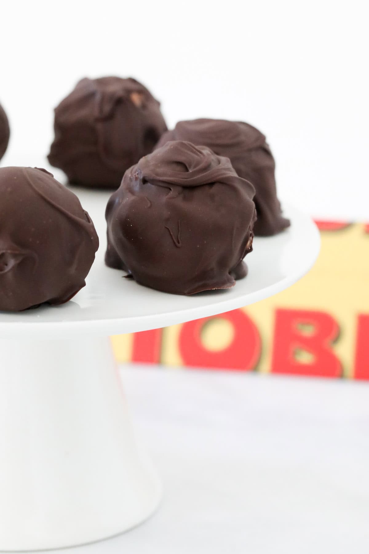 Chocolate coated cheesecake balls on a white cake stand.