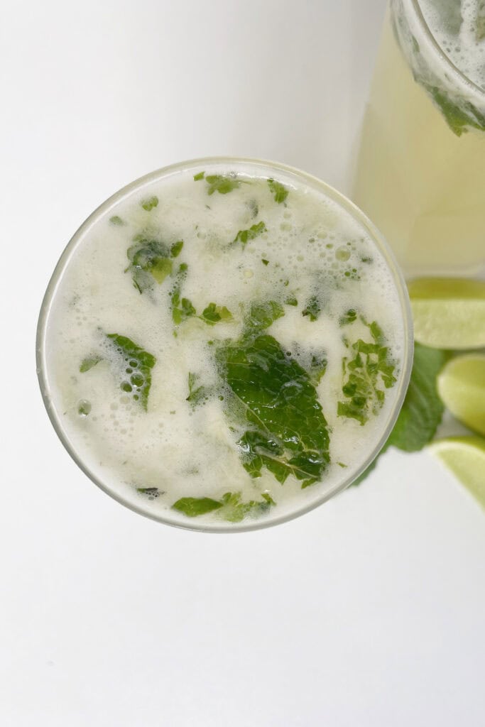 Overhead view of a mojito in a tall glass. In the background is lime and mint pieces.