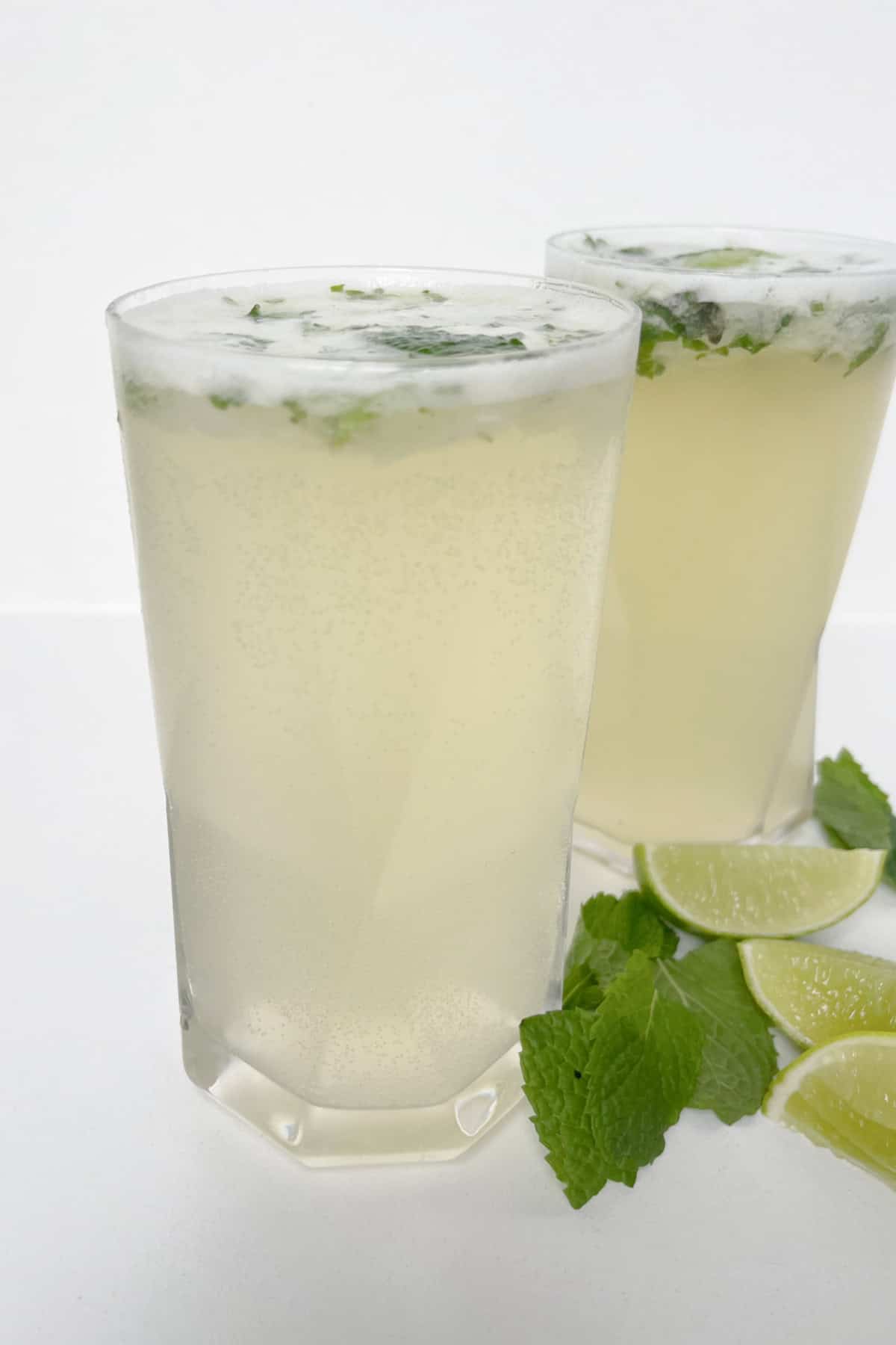 Side view of two glasses filled with Mojito cocktails. Mint leaves and lime wedges are sitting next to the glasses.