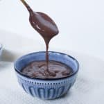 Chocolate custard drizzling from a gold spoon over the top of a blue bowl.