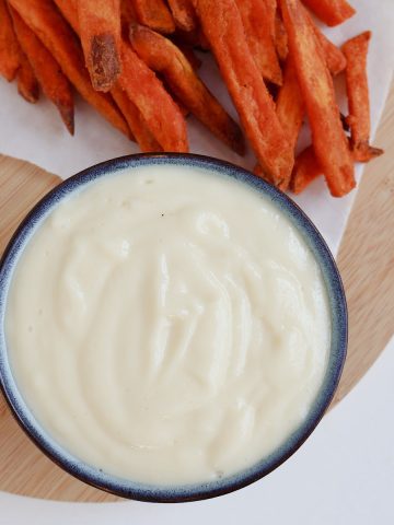 Aioli made in a thermomix in a blue bowl. Sitting on a timber board with sweet potato fries.