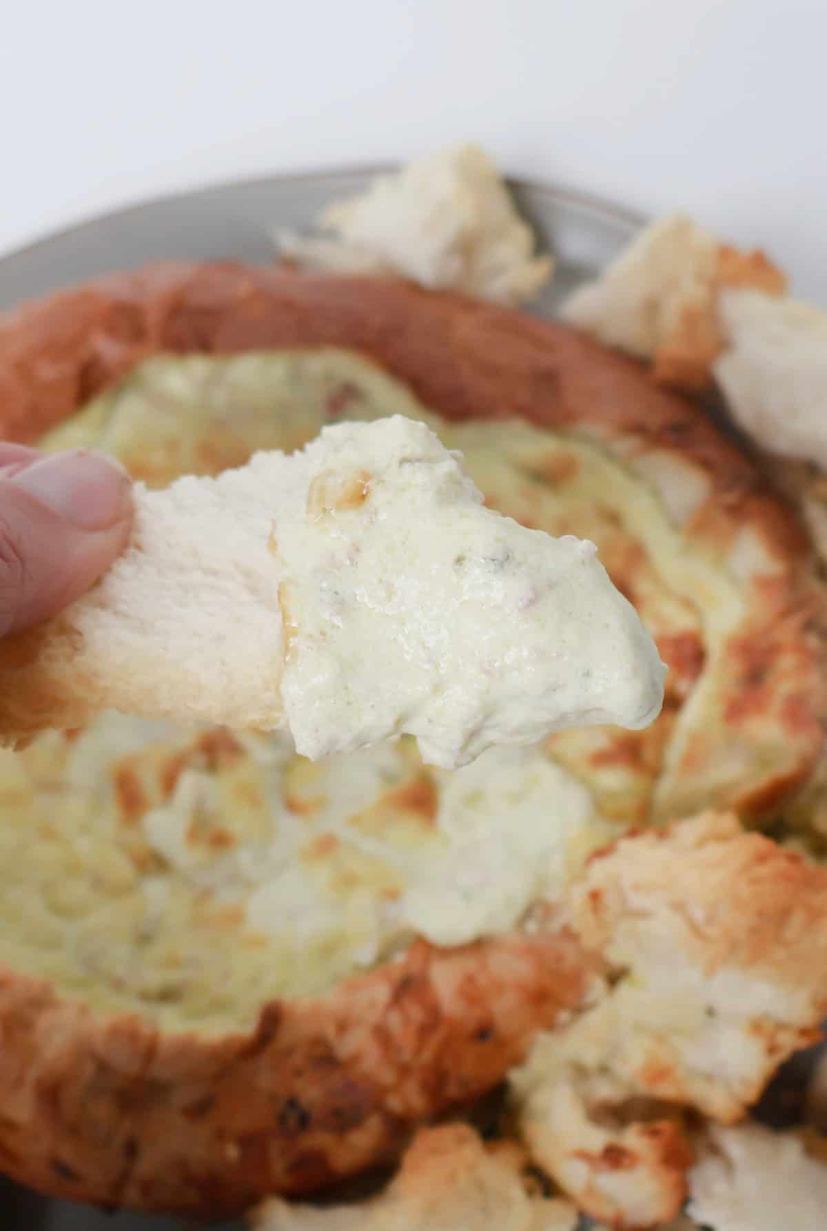 Adult holding a piece of toasted bread covered in bacon and cheese cob loaf dip.