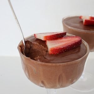 Chocolate Mousse topped with strawberries in a glass. A silver spoon is sticking out of it and a scoop is missing.