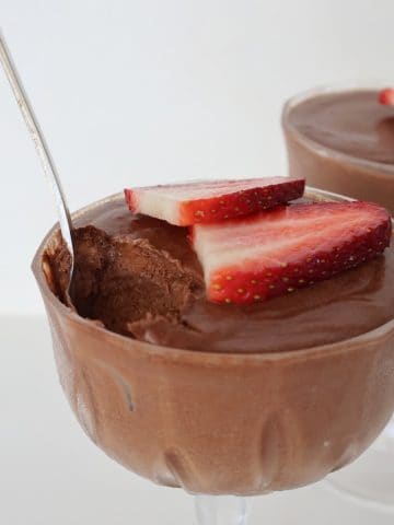 Chocolate Mousse topped with strawberries in a glass. A silver spoon is sticking out of it and a scoop is missing.