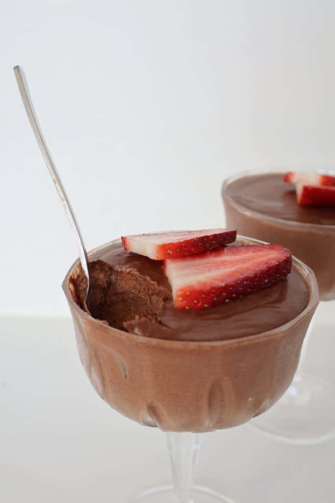 Chocolate Mousse topped with strawberries in a glass. A silver spoon is sticking out of it and a scoop is missing.