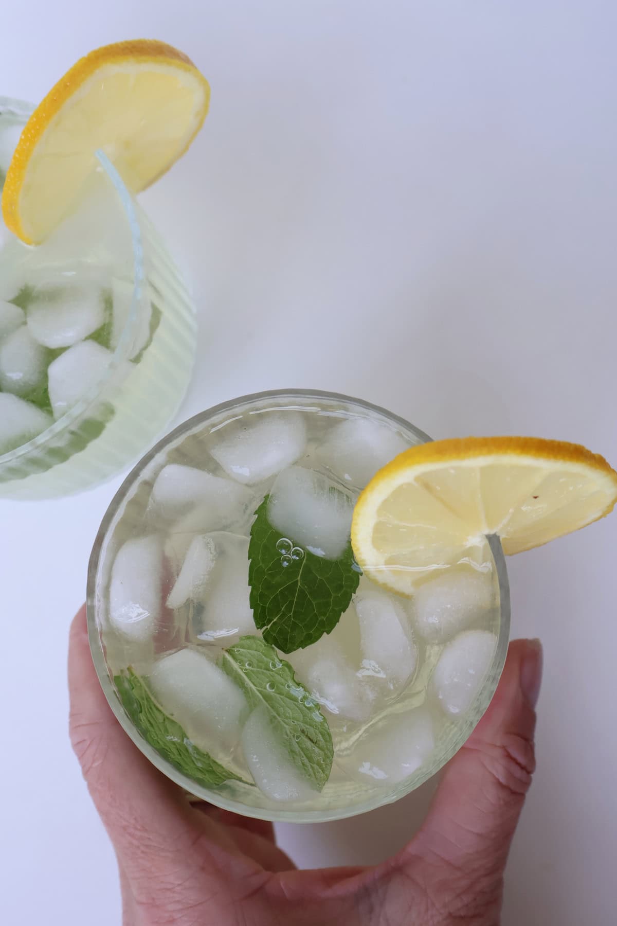 overhead view of Limoncello Spritz garnished with a slice of lemon being held by an adult hand.