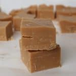 Two pieces of salted caramel fudge sitting on top of each other. In the background is more pieces of fudge.