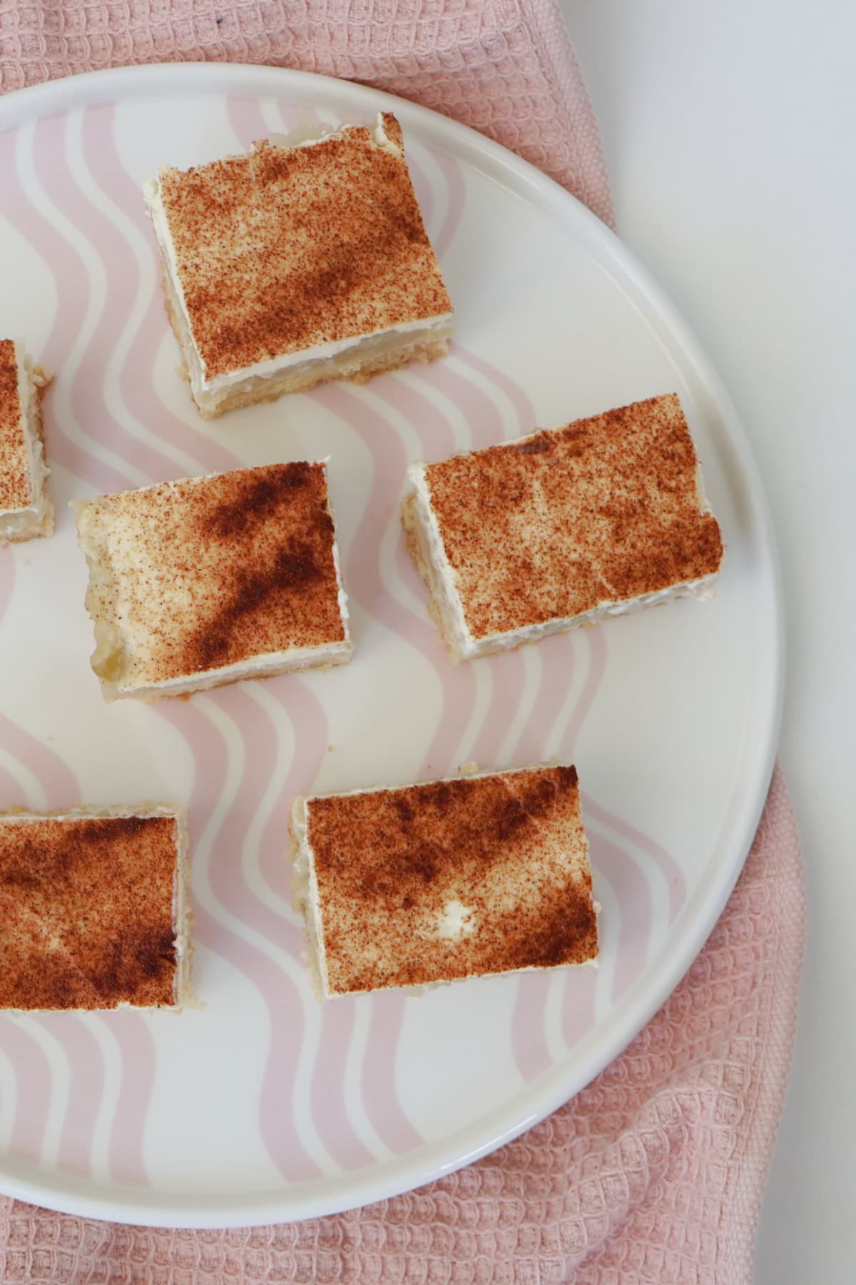 Overhead view of Slices of Apple and Sour Cream Slice sitting on a pink striped plate.
