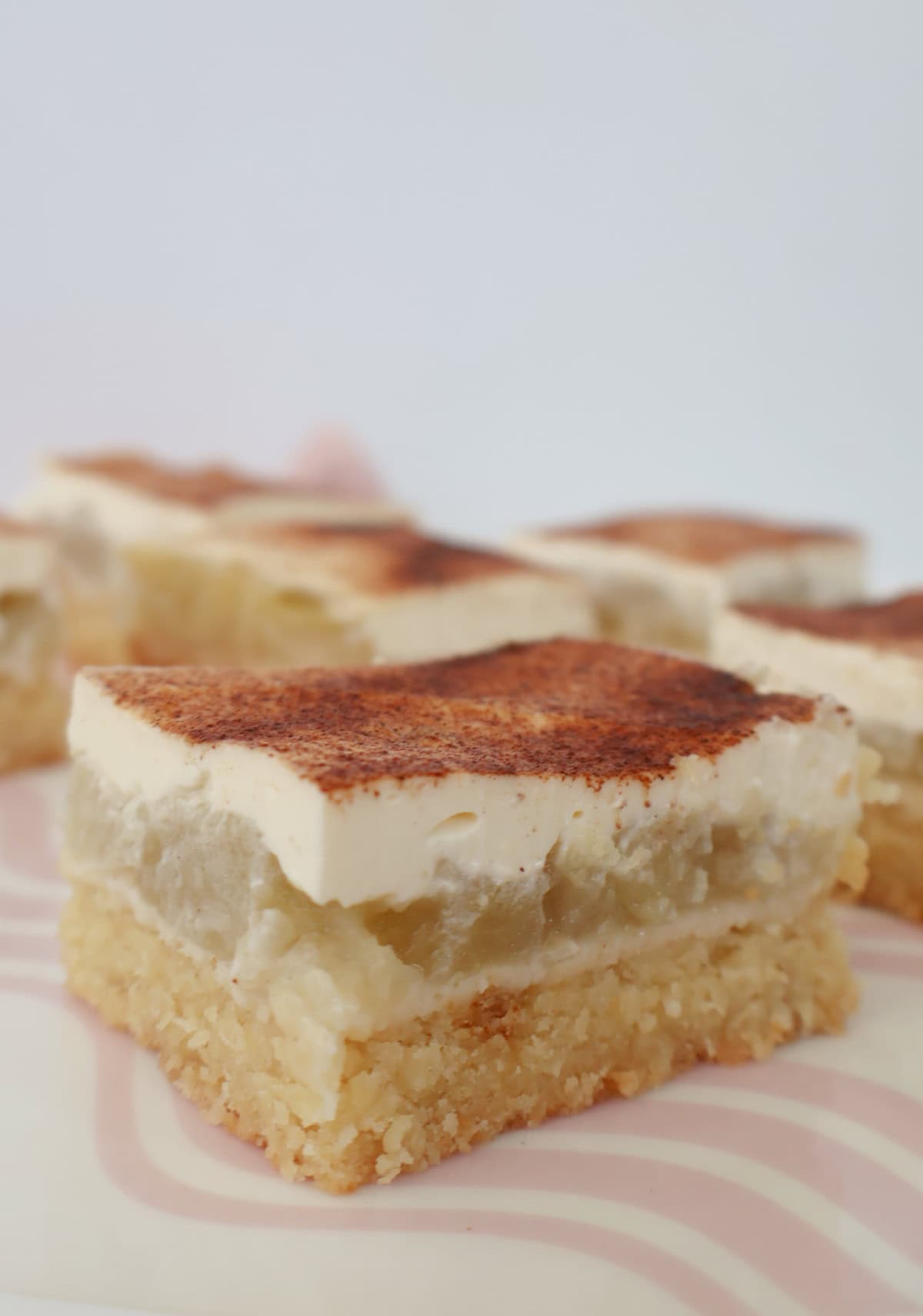 Close up of Slices of Apple and Sour Cream Slice sitting on a pink striped plate.
