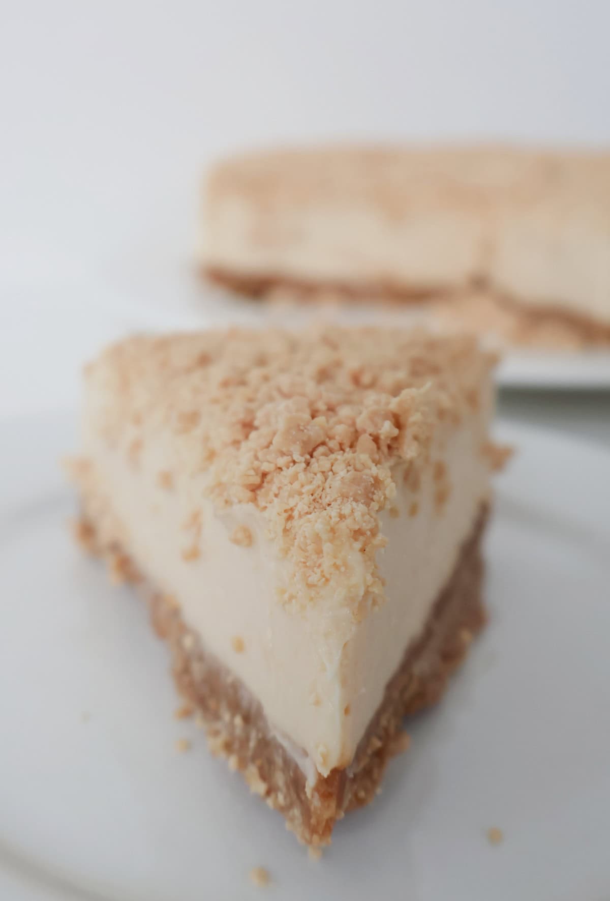 Front view of a slice of caramilk cheesecake on a white plate. In the background is the rest of caramilk cheesecake.