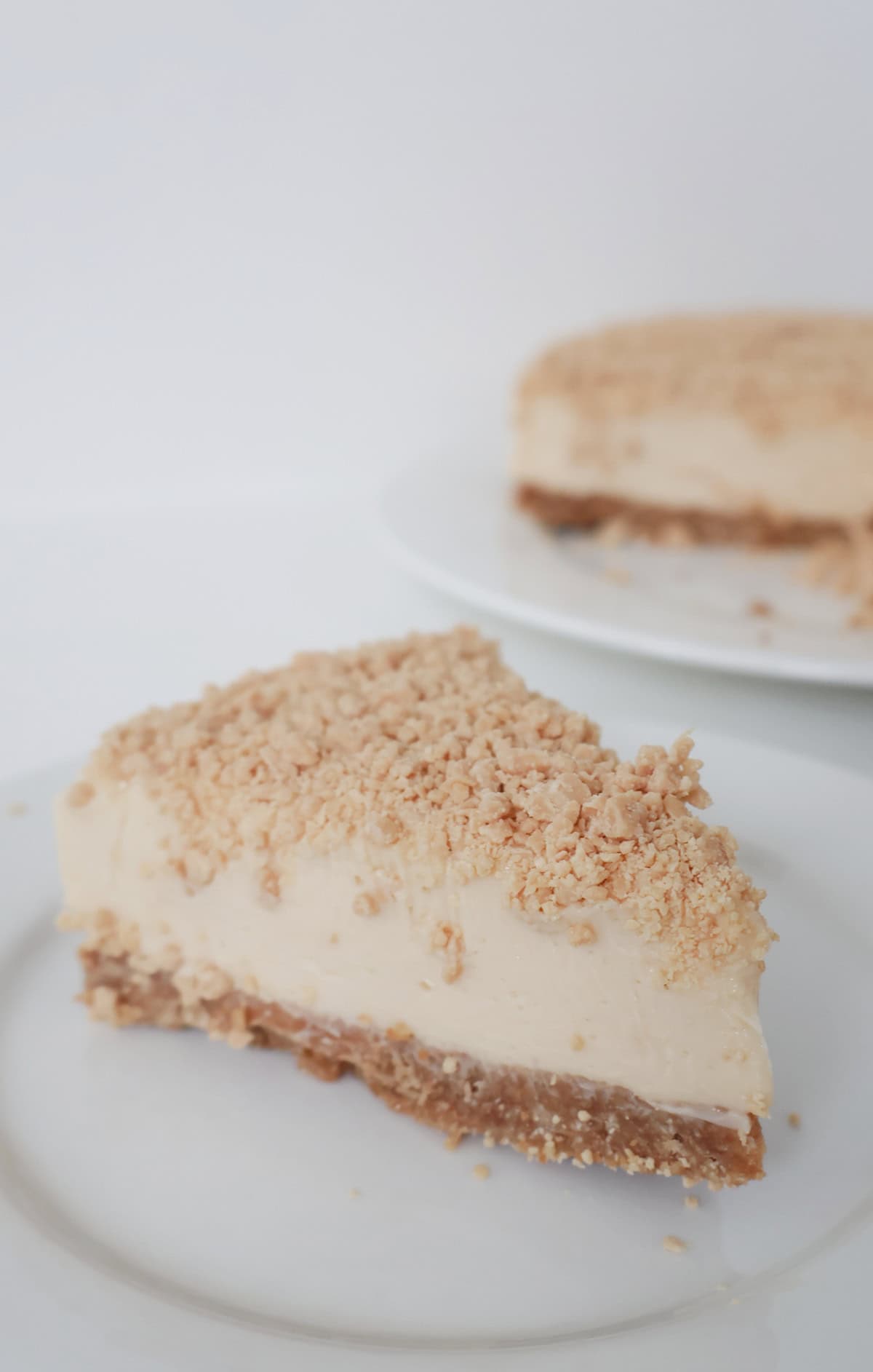 Slice of Caramilk Cheesecake on a white plate. In the background is the rest of the cheesecake.